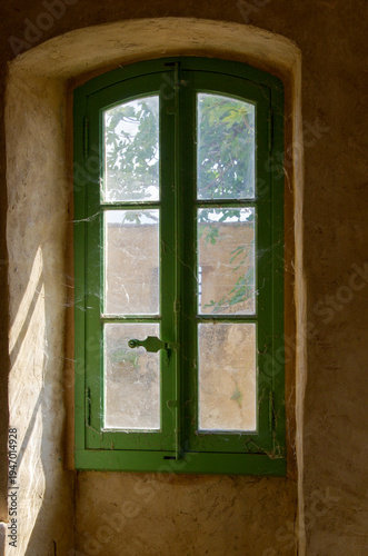 Old green window with cobwebs in stone wall
