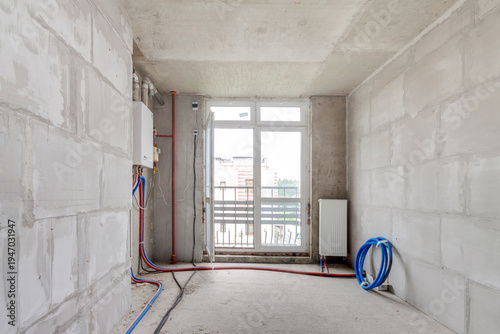 Empty unfinished apartment in new residential building before renovation with gas boiler and heating pipes