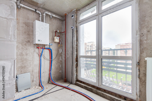 Gas boiler and heating pipes installed near large window in modern apartment interior