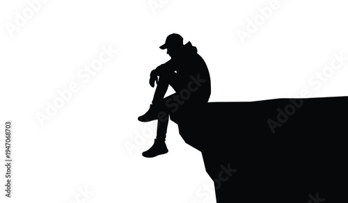 A silhouette of a lonely person wearing a cap sitting on the edge of a high cliff looking down