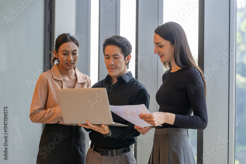 Group diverse business people standing together in modern office looking at laptop screen discussing financial data report during corporate meeting professional teamwork startup collaboration success
