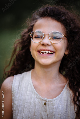 Close up portrait of a laughing little girl with curly hair wearing stylish golden glasses outdoors