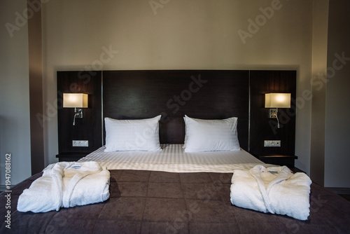 King size bed with white pillows and bathrobes in a modern luxury hotel room
