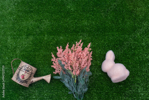 Easter flat lay with pink bunny, flowers, and vintage watering can on grass with copy space.