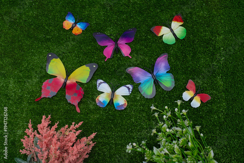 Spring flat lay with colorful decorative butterflies and flowers on green grass.