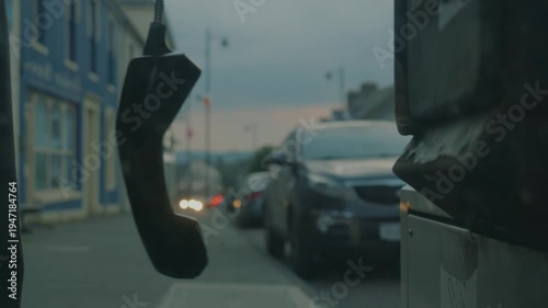 Abandoned telephone receiver hanging in a quiet Irish street at dusk, symbolizing disconnection and loneliness.