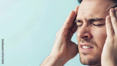 Stressed man suffering from a severe headache. A young male rubs his temples to relieve pain and migraine pressure. Healthcare concept for medical wellbeing care.