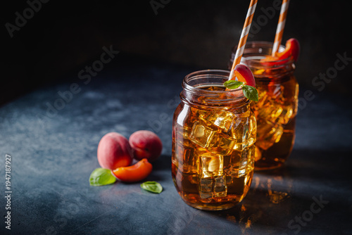Glass of peach or apricot iced tea with fruit slices against dark blue background