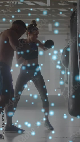 Vertical video: Coach with mitts cueing trainee hitting bag, blue overlay showing boxing technique