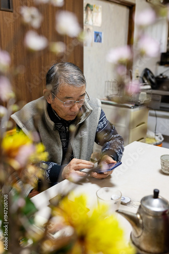 Senior mature middle aged man holding cell mobile phone using smartphone sitting at home on a chair, scrolling social media, checking financial apps, buying online, texting messages.