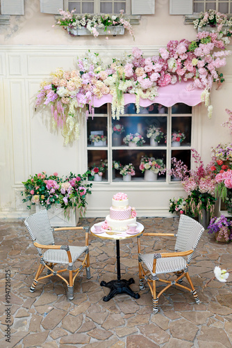 Wallpaper Mural Outdoor exterior terrace cafe with chairs and a small table with a cake, surrounded by abundant pink and pastel flowers decor. Festive floral decoration on a window facade creates spring atmosphere Torontodigital.ca