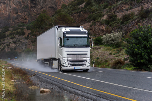 Quadro em tela Refrigerated semi truck driving on a wet road, raising a cloud of water