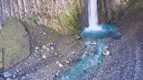 A fragment of a waterfall. A stream of water falls from a high cliff into a mountain river.