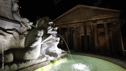 Close-up of the Fontana del Pantheon at night. The camera captures water pouring from the ancient marble sculpture in the foreground, while the majestic columns of the Pantheon glow in the soft-focus.