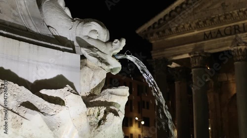 Real-time footage focusing on the intricate details of the Fontana del Pantheon. The camera captures water streaming from the mouth of a marble dolphin sculpture, with the softly lit facade.