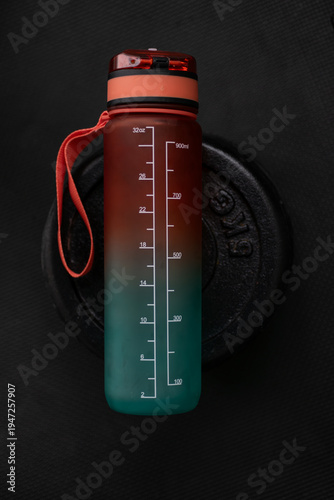 Canvastavla Reusable gym water bottle with measurement scale standing on barbell weight plate