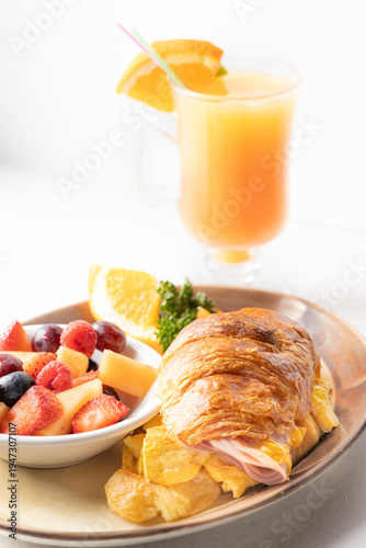 Breakfast croissant sandwich with eggs, ham and fresh fruit