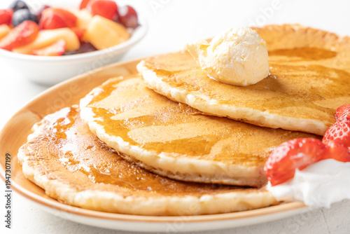 stack of pancakes with butter and maple syrup and strawberries