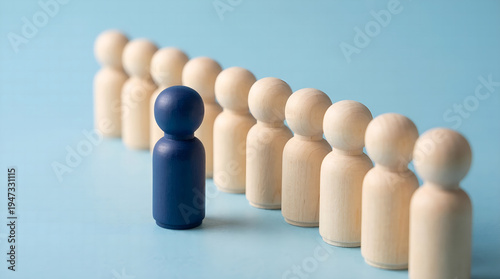 A distinct blue wooden human figure stands out in a structured line of identical natural wooden figurines, symbolizing individuality, leadership, and breaking from the norm within a group dynamic