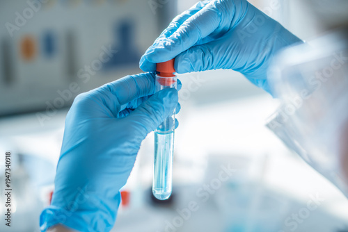 Closeup of gloved hands handling a test tube with clear solution in a bright scientific lab environment. Laboratory testing, diagnostics, and biotechnology research for medical advancements
