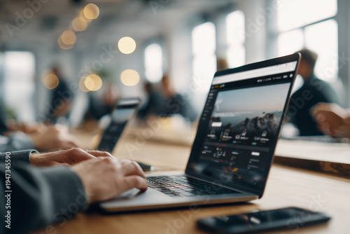 Person working on laptop with travel website open in modern office setting surrounded by blurred coworkers and ambient lighting creating productive atmosphere