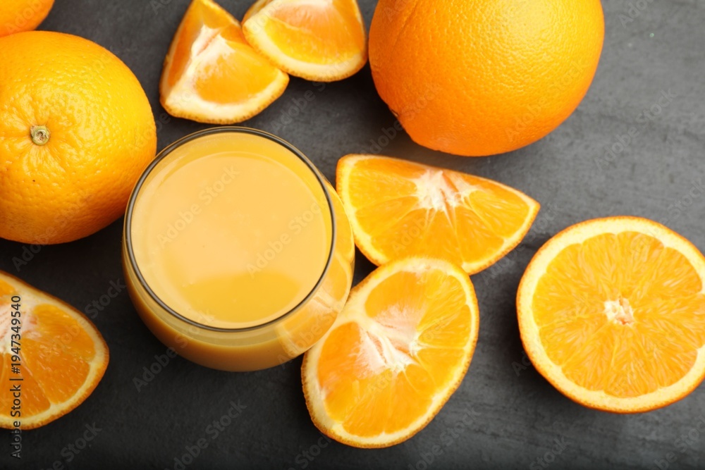 Fototapeta premium Citrus juice in glass and fresh oranges on black table, flat lay