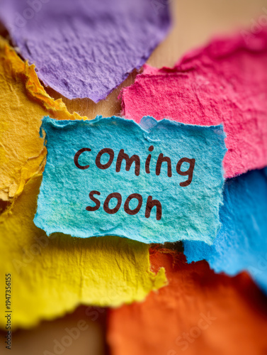 Colorful torn paper pieces with handwritten message coming soon on textured blue paper symbolizing anticipation and upcoming events announcement