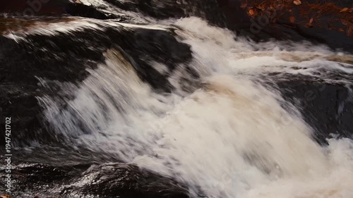 Powerful waterfall rushing over dark river rocks, close up of white water rapids with motion blur, scenic natural stream in autumn forest