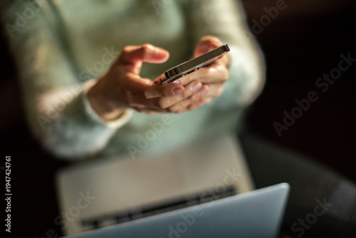 Person texting on smartphone while working on laptop at home