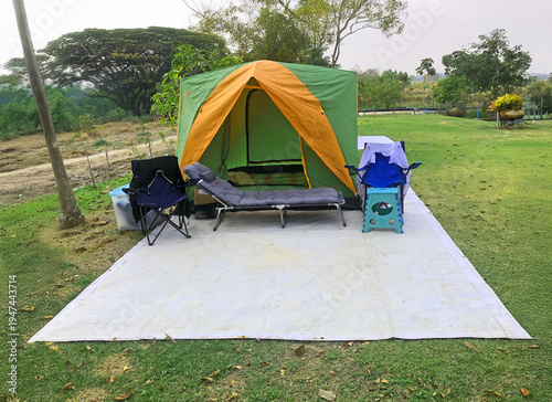 A tent and camping equipment are spread out on a white tarp on the lawn