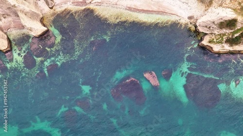 Scenic aerial view of a rugged coastal landscape featuring sea waves, rocky cliffs, clear blue water and untouched nature.