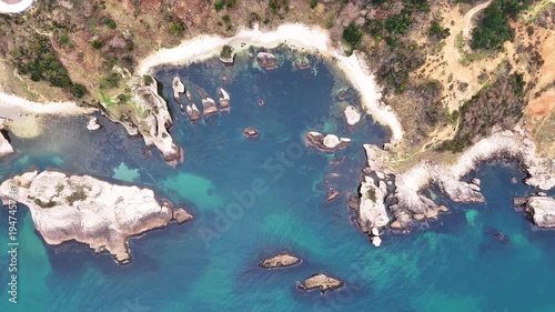 Scenic aerial view of a rugged coastal landscape featuring sea waves, rocky cliffs, clear blue water and untouched nature.