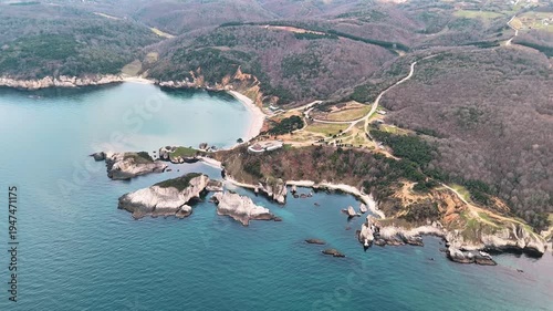 Scenic aerial view of a rugged coastal landscape featuring sea waves, rocky cliffs, clear blue water and untouched nature.