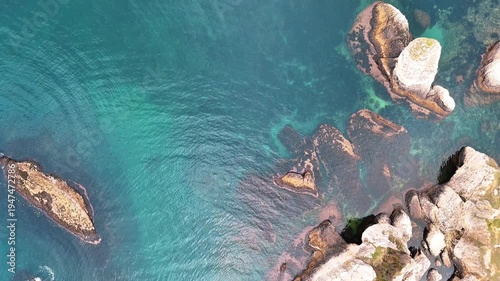 Scenic aerial view of a rugged coastal landscape featuring sea waves, rocky cliffs, clear blue water and untouched nature.