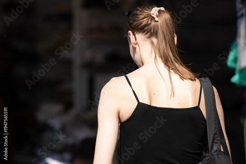 Vászonkép Female traveler in black tank top shopping in market, pedestrian walking in harsh sunlight, skin texture, rear view, at Chatuchak Market