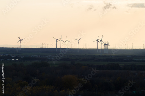 Wind turbines on horizon at sunset, renewable energy landscape with silhouettes against warm orange sky