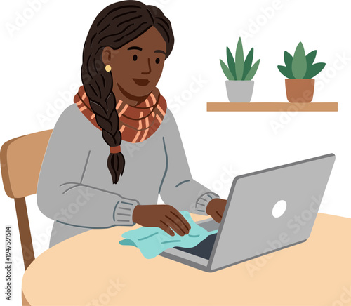 A woman sits at a table working on a laptop and wiping her hands with a cloth indoors.