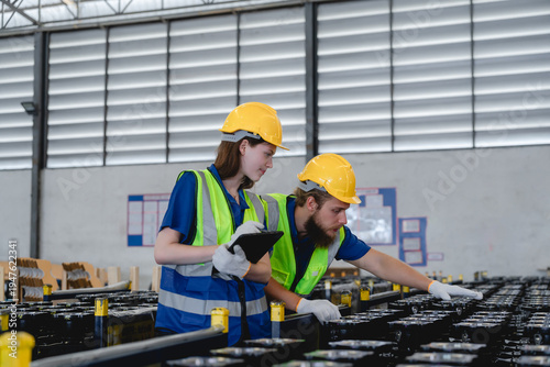 Industrial factory warehouse environment with Caucasian logistics workers wearing safety helmets and reflective vests while inspecting automotive metal components. warehouse management concept.