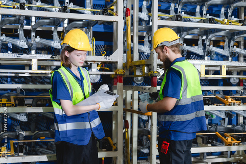 Industrial warehouse environment with Caucasian logistics workers wearing safety helmets and reflective vests while inspecting industrial components. Industrial parts warehouse concept.