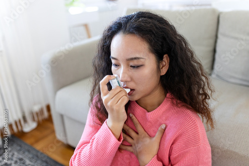 Tableau sur toile Young Asian woman using an asthma inhaler to treat breathing difficulty at home