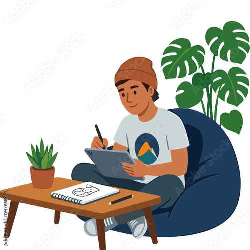 A man sits on a bean bag chair drawing on a tablet with a plant and notebook nearby indoors.