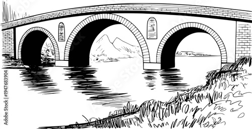 Black and white of an arched stone bridge over a river with mountains in the background