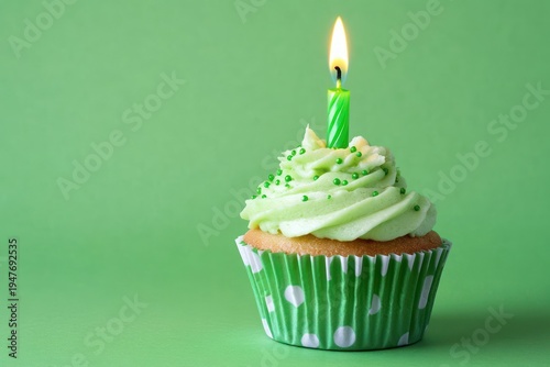 single cupcake with green buttercream swirl, green sprinkles and a lit green candle in a polka dot wrapper on a green background, cheerful celebratory mood