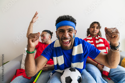 Group of excited multiethnic friends watching soccer match at home, screaming and celebrating a goal