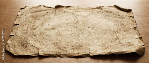 Aged yellowed and torn parchment paper laid flat on a wooden table surface