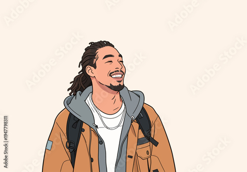 A young man with a big smile stands indoors. He wears a brown jacket and a gray hoodie. His backpack is slung over one shoulder.