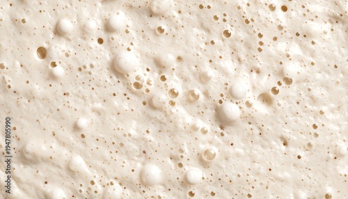 Close-up of a light-brown, bubbling substance, possibly a fermenting dough. Small and large bubbles create a textured surface