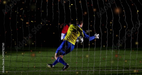 фотографія Diving goalkeeper in yellow jersey reaching for ball on night pitch, with gloves