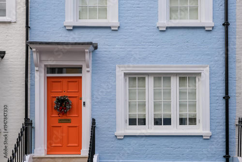 London, UK – A vibrant orange front door contrasting with a light blue facade in Chelsea, featuring a traditional winter wreath, showcasing the colorful residential charm of South West London.