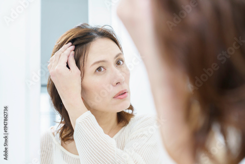 鏡を見て、薄毛を気にするミドルエイジの日本人女性